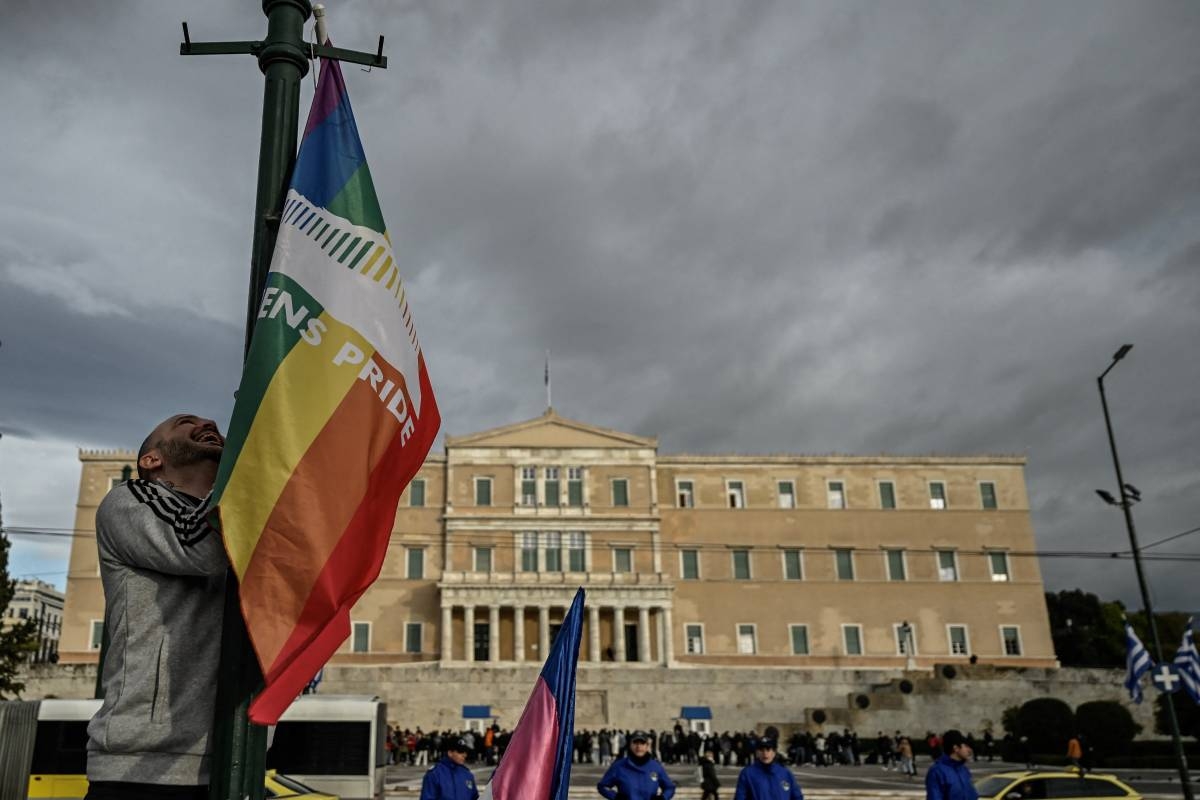 A person hangs a LGBTQ pride flag on a light pole outside the Greek Parliament during a gathering with fellow supporters of the LGBTQ community as lawmakers vote on a same-sex marriage and adoption for same-sex couples bill on February 15, 2024 in Athens. Greece's Parliament was set to legalise same-sex marriage and adoption today, a landmark reform promoted by the conservative government over the opposition of the country's powerful Orthodox Church. (Photo by Aris MESSINIS / AFP)