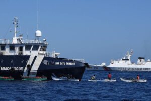 This photo taken on February 15, 2024 shows Filipino fishermen aboard their wooden boats queueing for free fuel beside the Philippine Bureau of Fisheries and Aquatic Resources (BFAR) ship BRP Datu Tamblot (L) as a Chinese coast guard ship (background R) monitors near the China-controlled Scarborough Shoal, in disputed waters of the South China Sea. The Philippines on February 17 accused Chinese coast guard vessels of "dangerous" manoeuvres for attempting to block a Filipino vessel dropping supplies to fishermen at a reef off the Southeast Asian nation's coast. (Photo by Ted ALJIBE / AFP) / “The erroneous mention[s] appearing in the metadata of this photo by Ted ALJIBE has been modified in AFP systems in the following manner: [At sea] instead of [Scarborough Shoal]. Please immediately remove the erroneous mention[s] from all your online services and delete it (them) from your servers. If you have been authorized by AFP to distribute it (them) to third parties, please ensure that the same actions are carried out by them. Failure to promptly comply with these instructions will entail liability on your part for any continued or post notification usage. Therefore we thank you very much for all your attention and prompt action. We are sorry for the inconvenience this notification may cause and remain at your disposal for any further information you may require.”