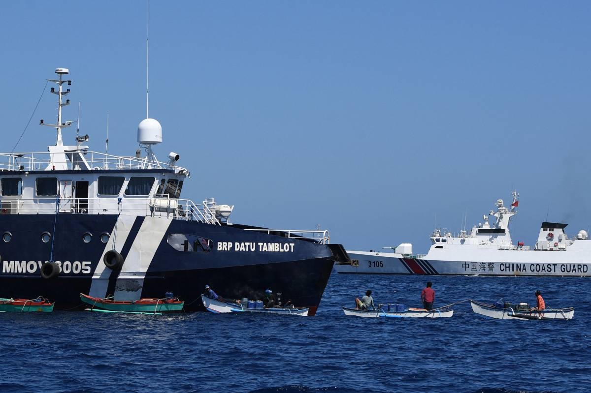 This photo taken on February 15, 2024 shows Filipino fishermen aboard their wooden boats queueing for free fuel beside the Philippine Bureau of Fisheries and Aquatic Resources (BFAR) ship BRP Datu Tamblot (L) as a Chinese coast guard ship (background R) monitors near the China-controlled Scarborough Shoal, in disputed waters of the South China Sea. The Philippines on February 17 accused Chinese coast guard vessels of "dangerous" manoeuvres for attempting to block a Filipino vessel dropping supplies to fishermen at a reef off the Southeast Asian nation's coast. (Photo by Ted ALJIBE / AFP) / “The erroneous mention[s] appearing in the metadata of this photo by Ted ALJIBE has been modified in AFP systems in the following manner: [At sea] instead of [Scarborough Shoal]. Please immediately remove the erroneous mention[s] from all your online services and delete it (them) from your servers. If you have been authorized by AFP to distribute it (them) to third parties, please ensure that the same actions are carried out by them. Failure to promptly comply with these instructions will entail liability on your part for any continued or post notification usage. Therefore we thank you very much for all your attention and prompt action. We are sorry for the inconvenience this notification may cause and remain at your disposal for any further information you may require.”