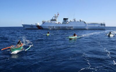 This photo taken on February 15, 2024 shows Filipino fishermen aboard their wooden boats sailing past a Chinese coast guard ship near the China-controlled Scarborough Shoal, in disputed waters of the South China Sea. AFP PHOTO