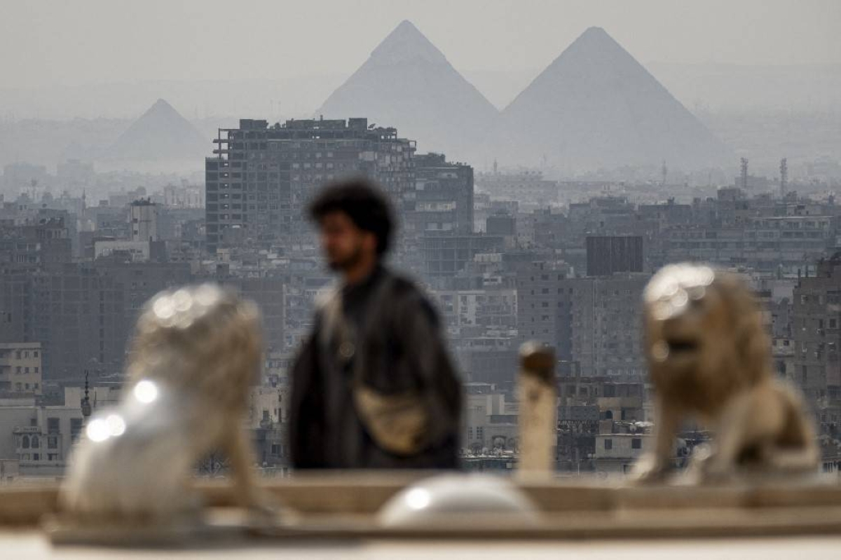 (From left) The Great Pyramid of Khufu (Cheops) and the Pyramids of Khafre (Chephren) and Menkaure (Menkheres) in Giza are visible in the background as a tourist walks at the promontory of the Cairo Citadel overlooking the skyline of Cairo and its twin city of Giza on February 19, 2024. AFP PHOTO
