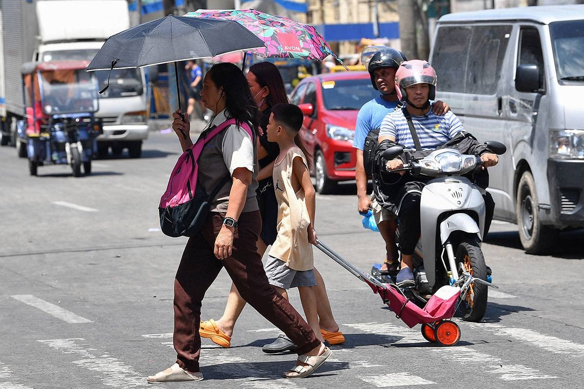 A family holding umbrellas to protect themselves from the sun walk across a street in Manila on April 25, 2024. Extreme heat is scorching parts of South and Southeast Asia, prompting health warnings from authorities as high temperatures are recorded across the region. Ted ALJIBE / AFP